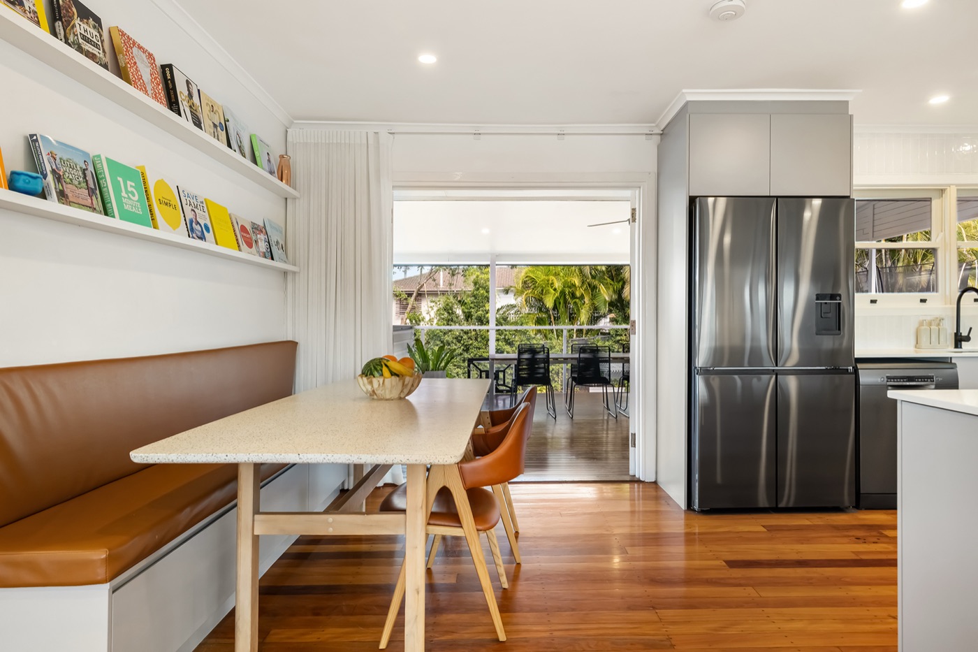 Dining area with a custom leather bench seat, stone-topped table and cookbook shelves, opening to the deck