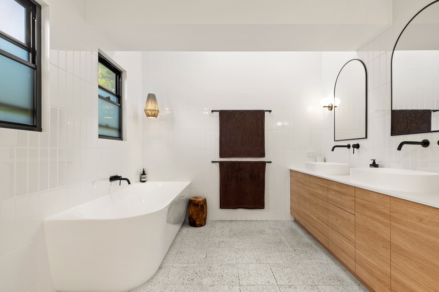 Ensuite with a freestanding bath, twin basins on a timber vanity, arched mirrors and black tapware