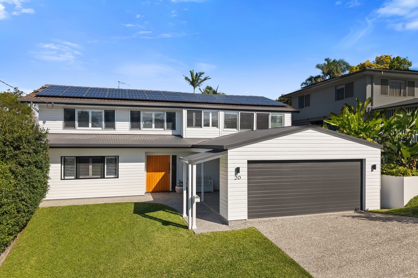 Street view of the white weatherboard facade with charcoal roof, rooftop solar panels, timber front door and double carport