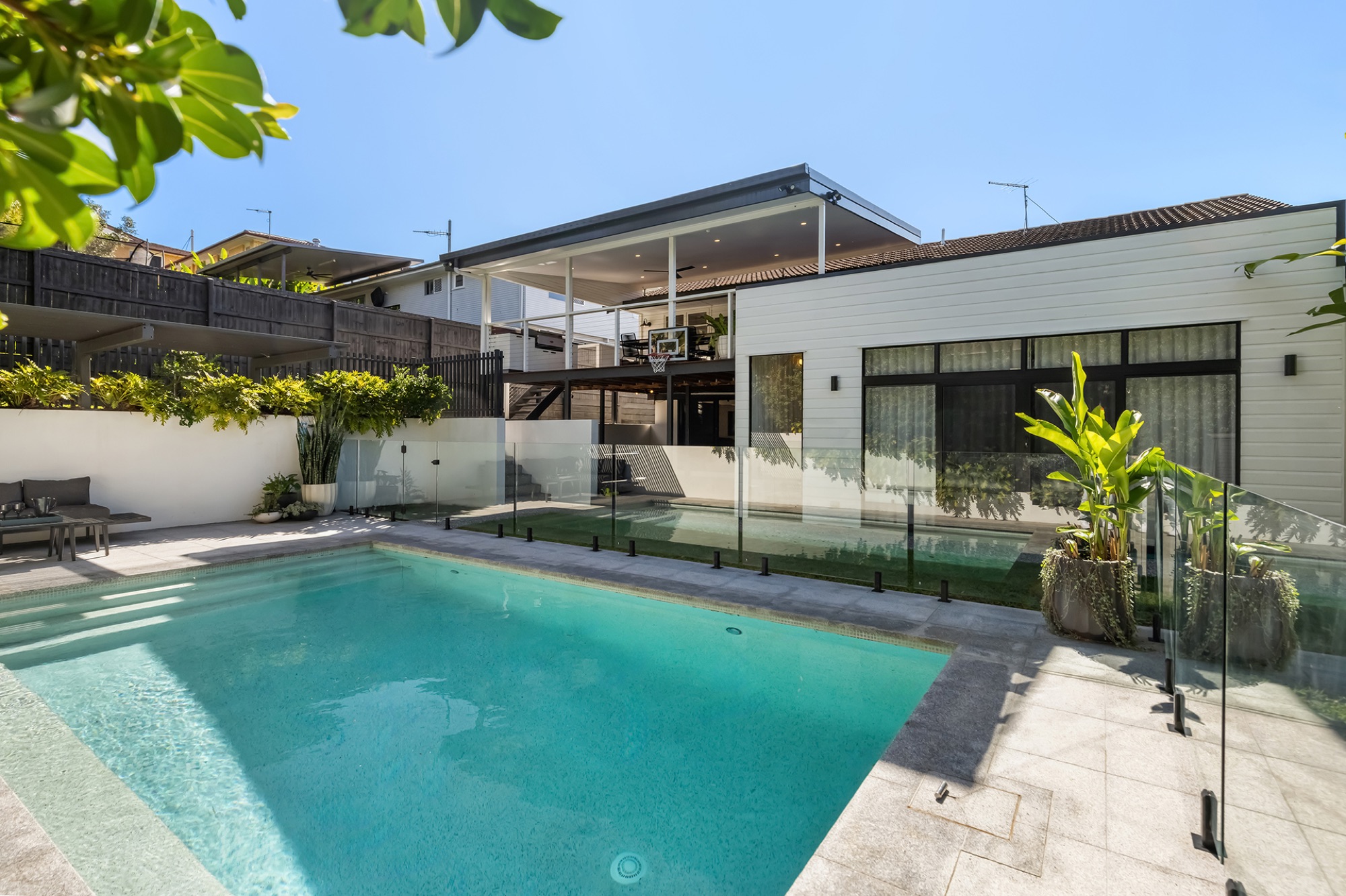 Rear of the renovated white weatherboard home at 20 Streeton Parade, with a heated saltwater pool, glass fencing and a covered upper deck
