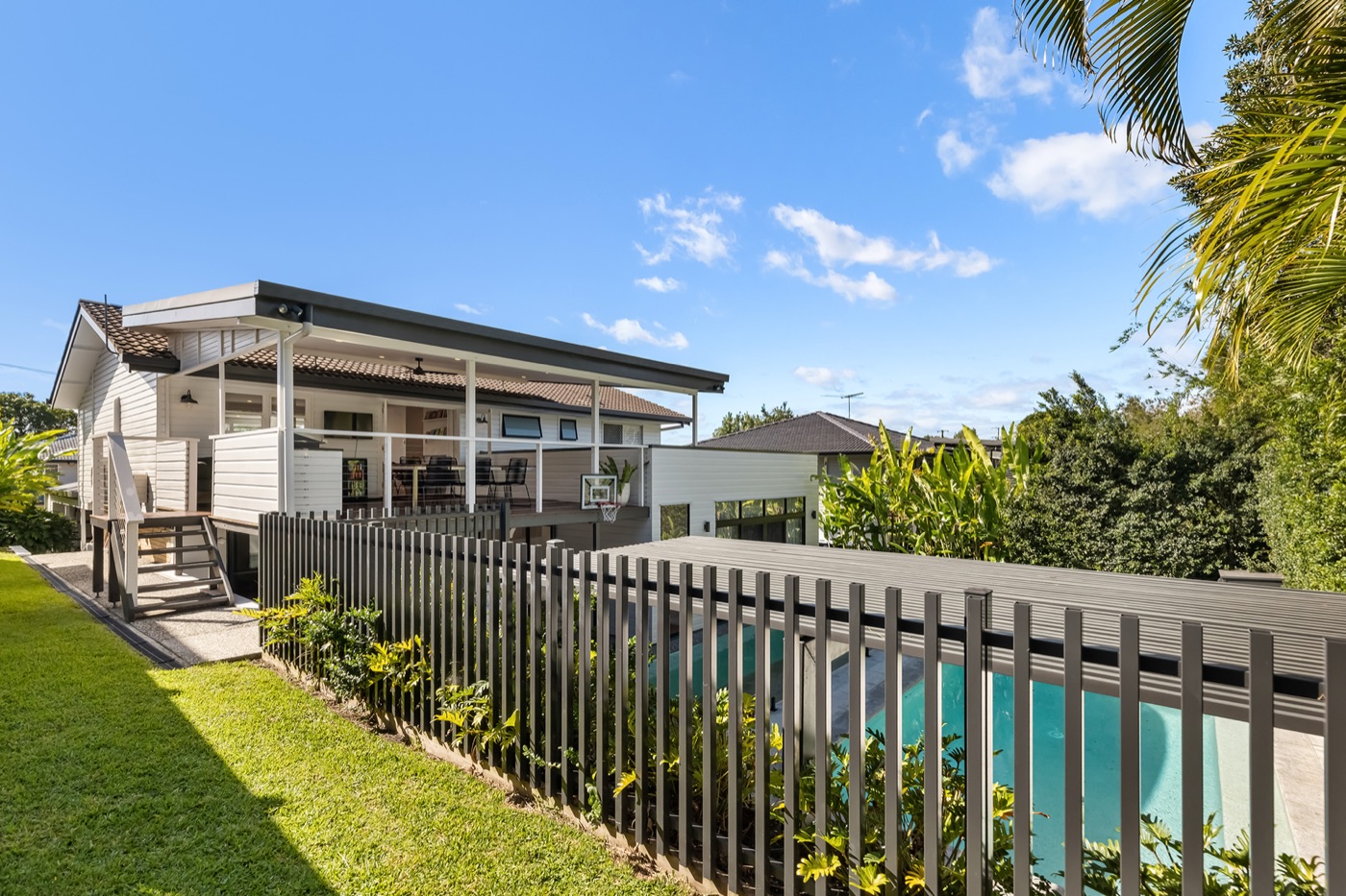 The house and heated pool seen from the level lawn, with the covered deck above and landscaped gardens on both sides