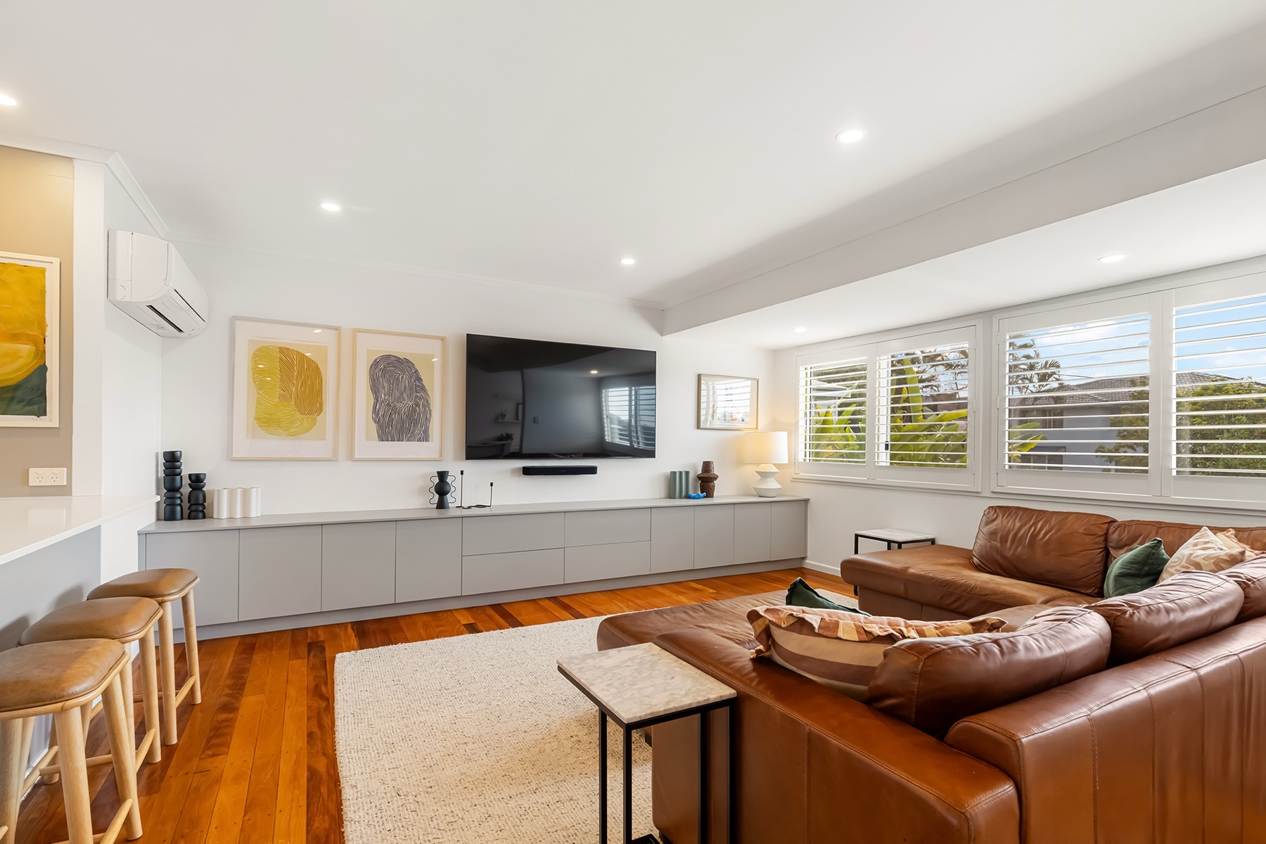 Upstairs open-plan living room with spotted-gum floors, plantation shutters, wall-hung television and custom joinery