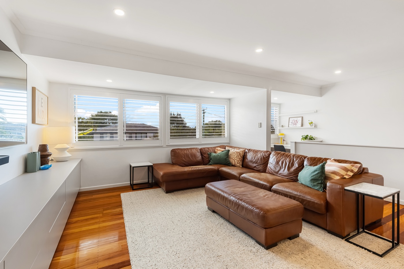 Second view of the upstairs lounge, with a large sectional sofa, wool rug and louvred windows to the treetops