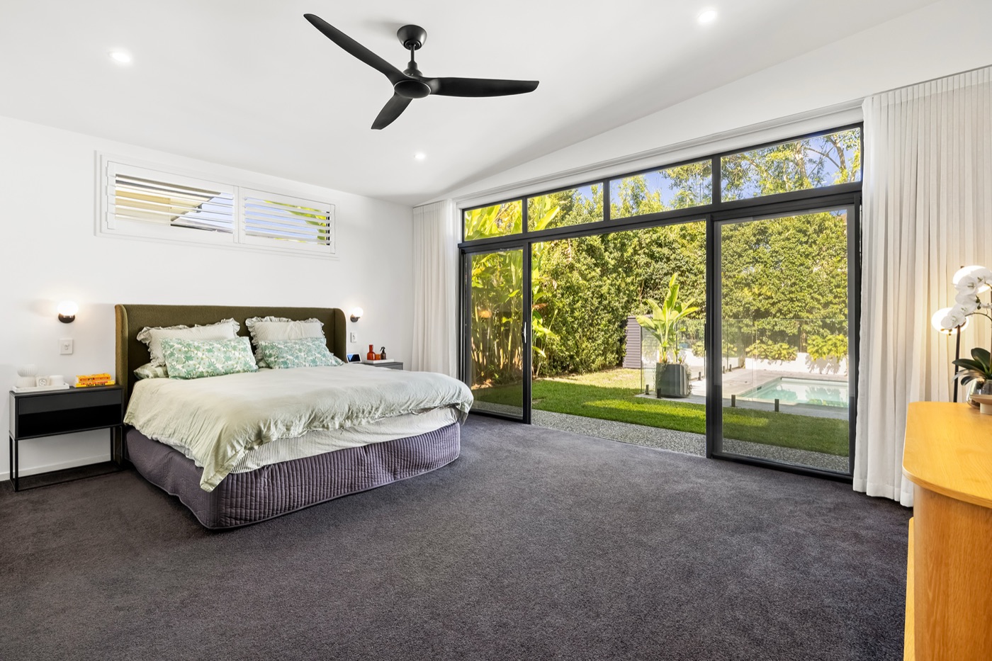 Master bedroom with a king bed and full-height sliding doors opening directly to the lawn and pool