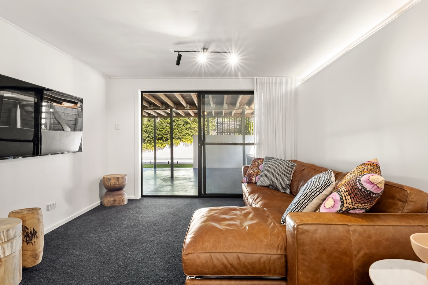 Downstairs rumpus and media room with a leather lounge, wall-mounted television and sliding door to the poolside terrace